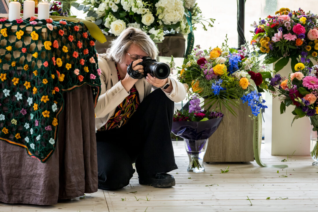 Afscheidsfotograaf maakt vanuit laag standpunt een foto van het bloemwerk