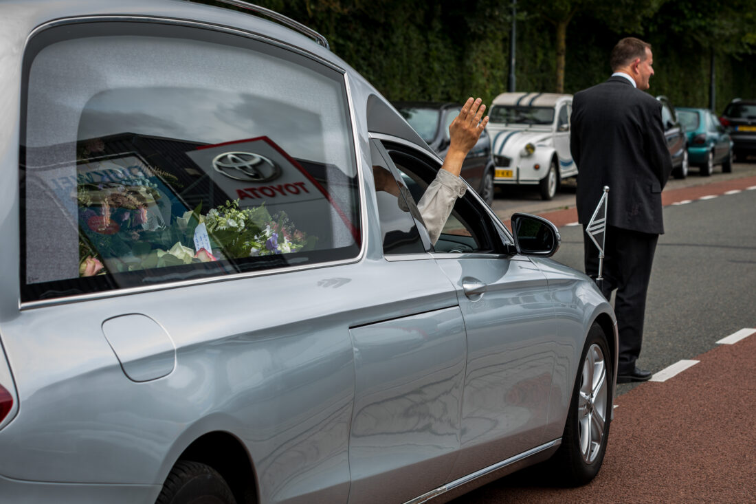 Zwaai door het open raampje van de rouwauto bij het vertrek naar de begraafplaats